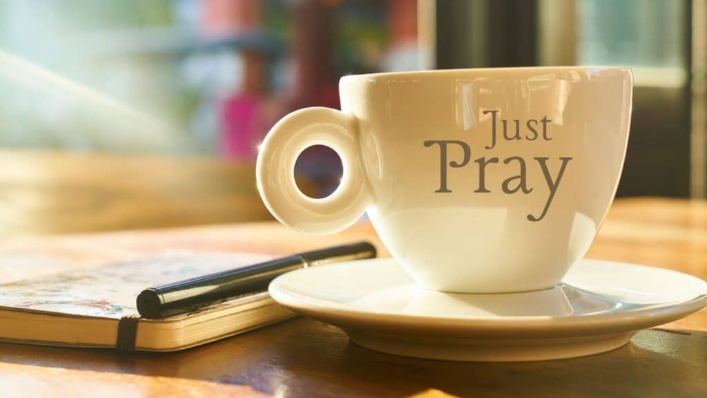 coffee cup that says just pray sitting next to a journal notebook