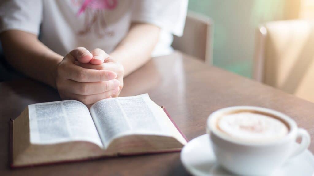woman praying over her Bible next to a cup of coffee
