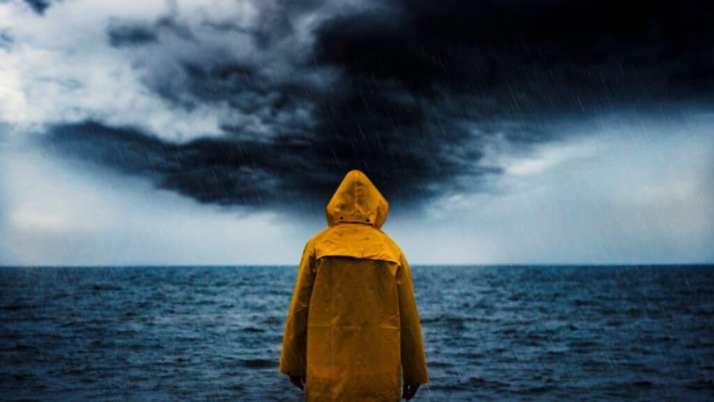 person in a rain jacket looking out over the ocean and the storms that is approaching