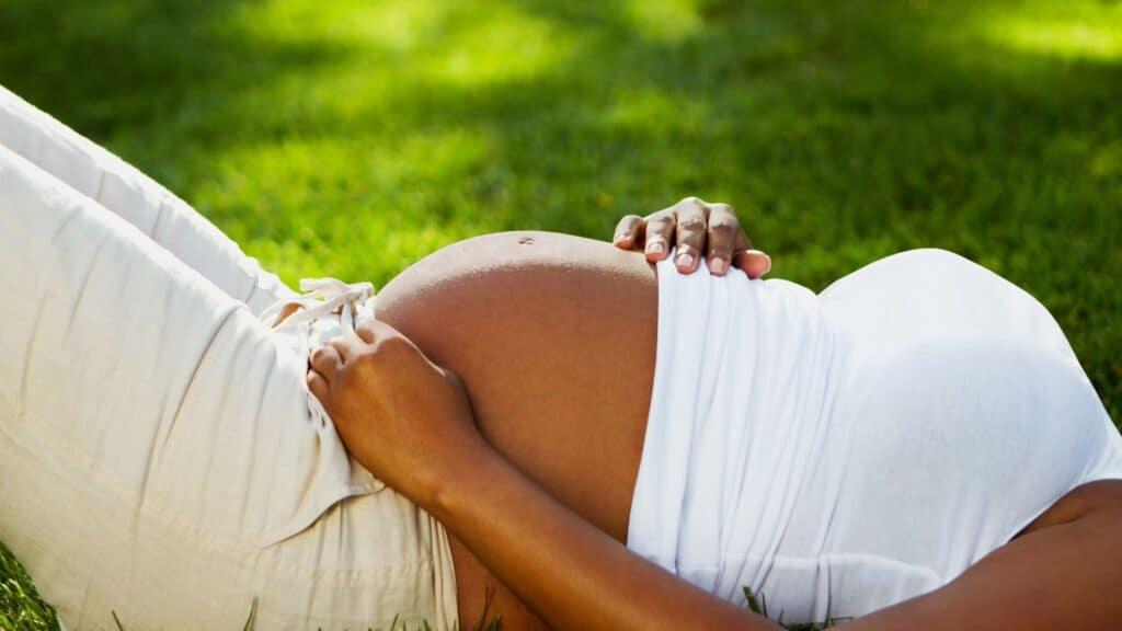 pregnant woman laying down outside in the grass with her hands over her belly