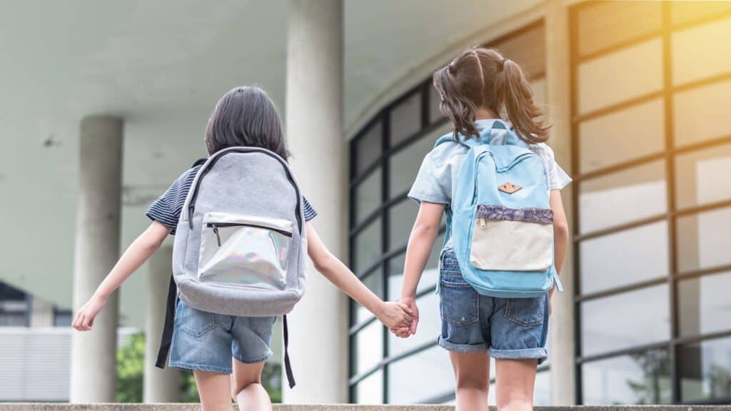two young girls walking into school with their backpacks on