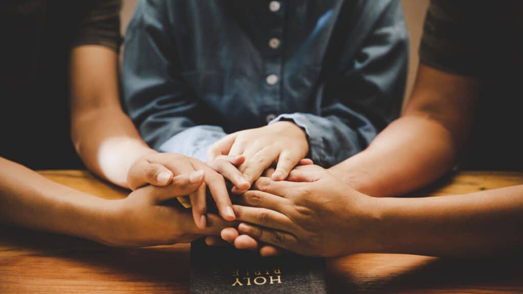 three people with with their hands locked together on a table as if praying together