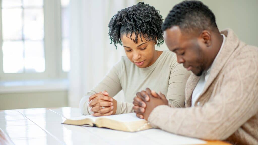 husband and wife sitting at the table praying over their bible