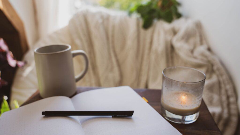 an open prayer journal laying on a table with a candle and coffee mug
